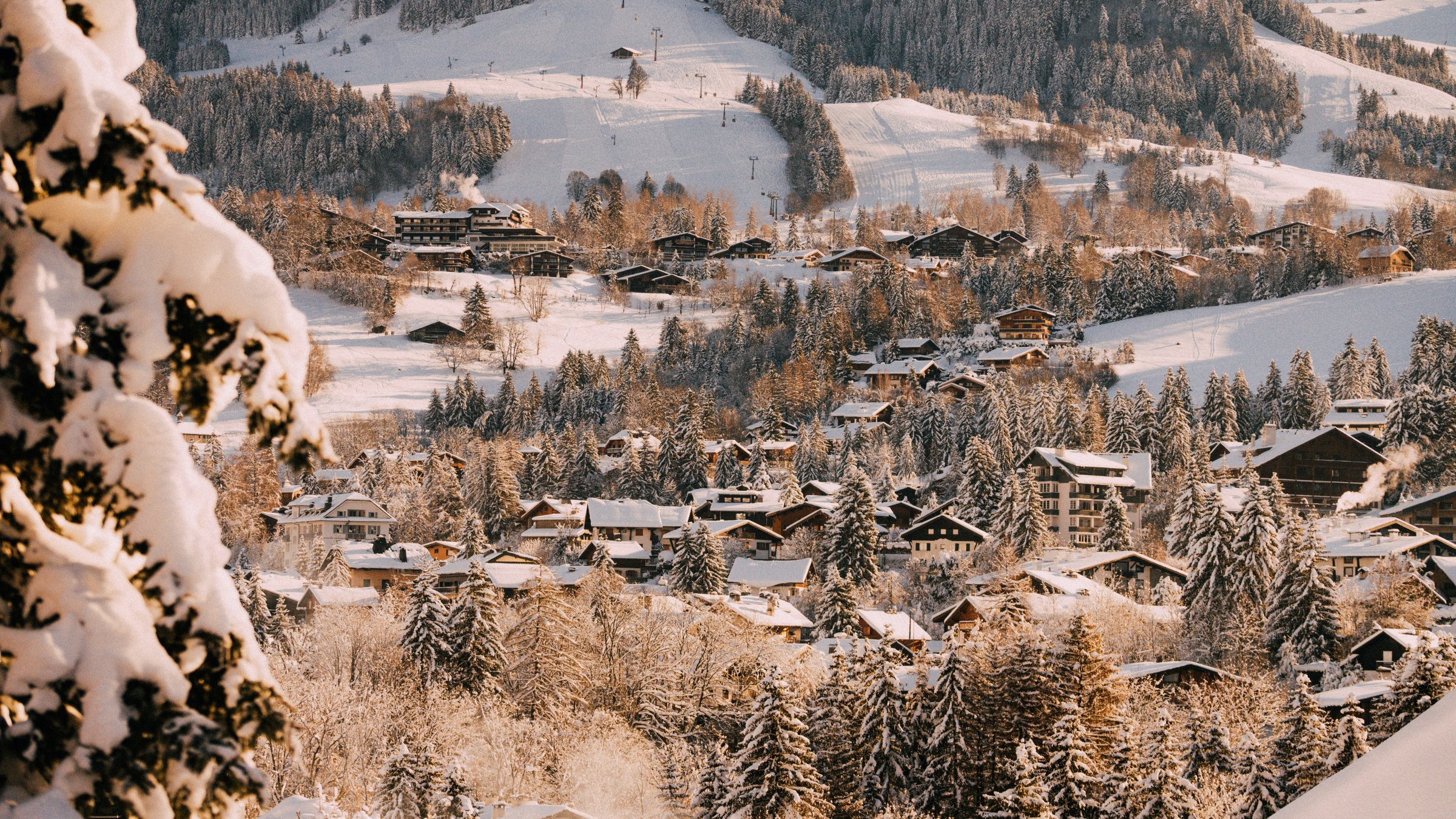 Le village de Megève sous la neige à la lumière dorée du matin, chalets, forêts et pistes de ski