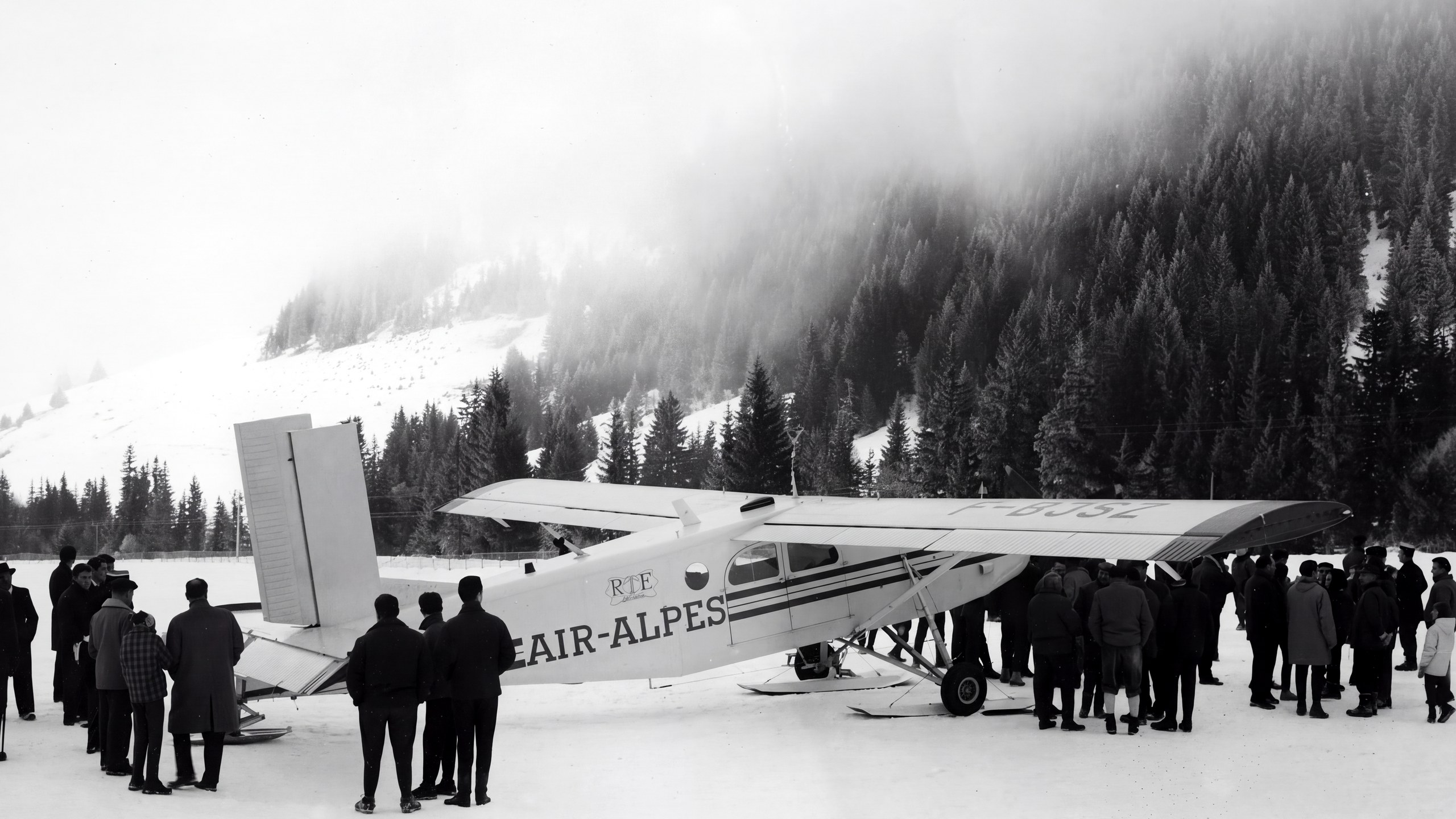 Photo d'archives en noir et blanc : un avion de la compagnie Air Alpes posé sur la neige de l'altiport de Megève, entouré de spectateurs