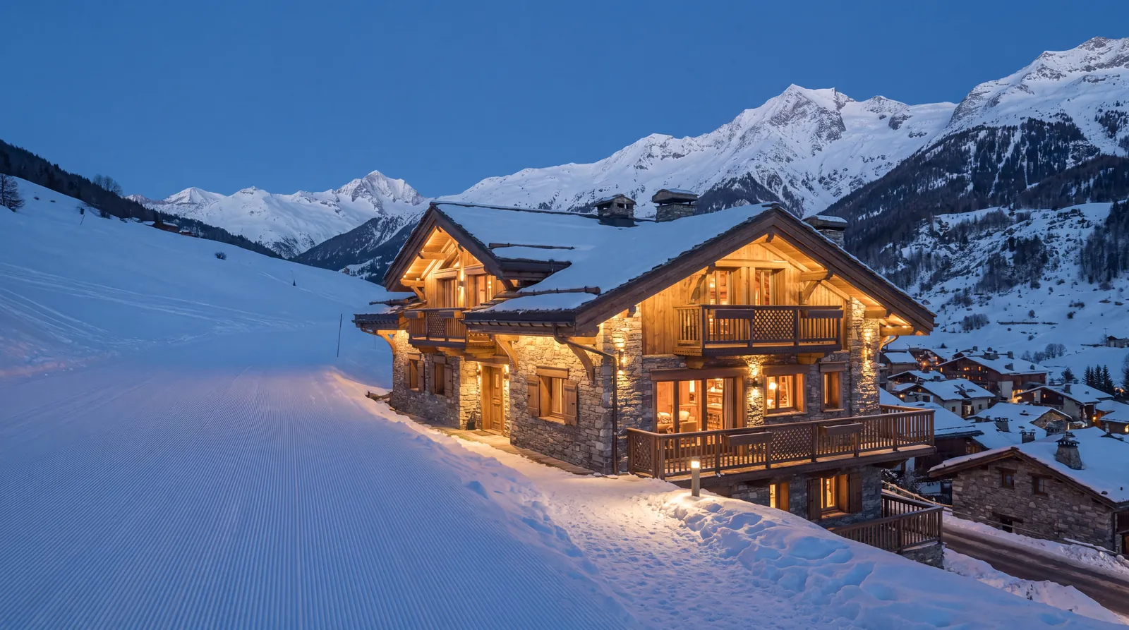 Chalet de pierre et de bois éclairé au pied d'une piste damée, à l'heure bleue