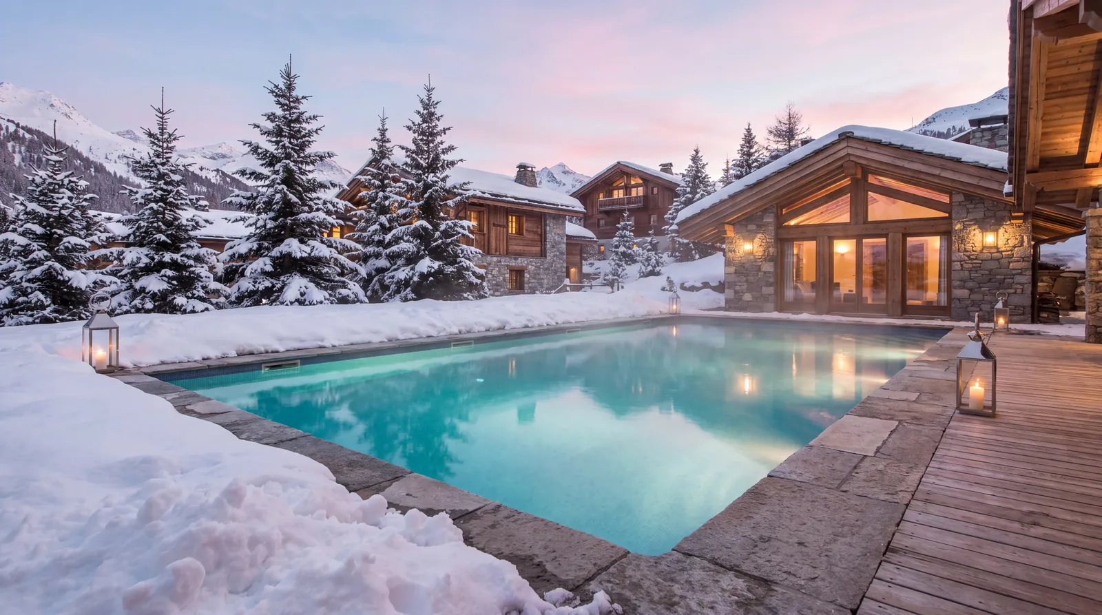 Piscine extérieure chauffée d'un chalet sous la neige, au crépuscule, face aux sommets