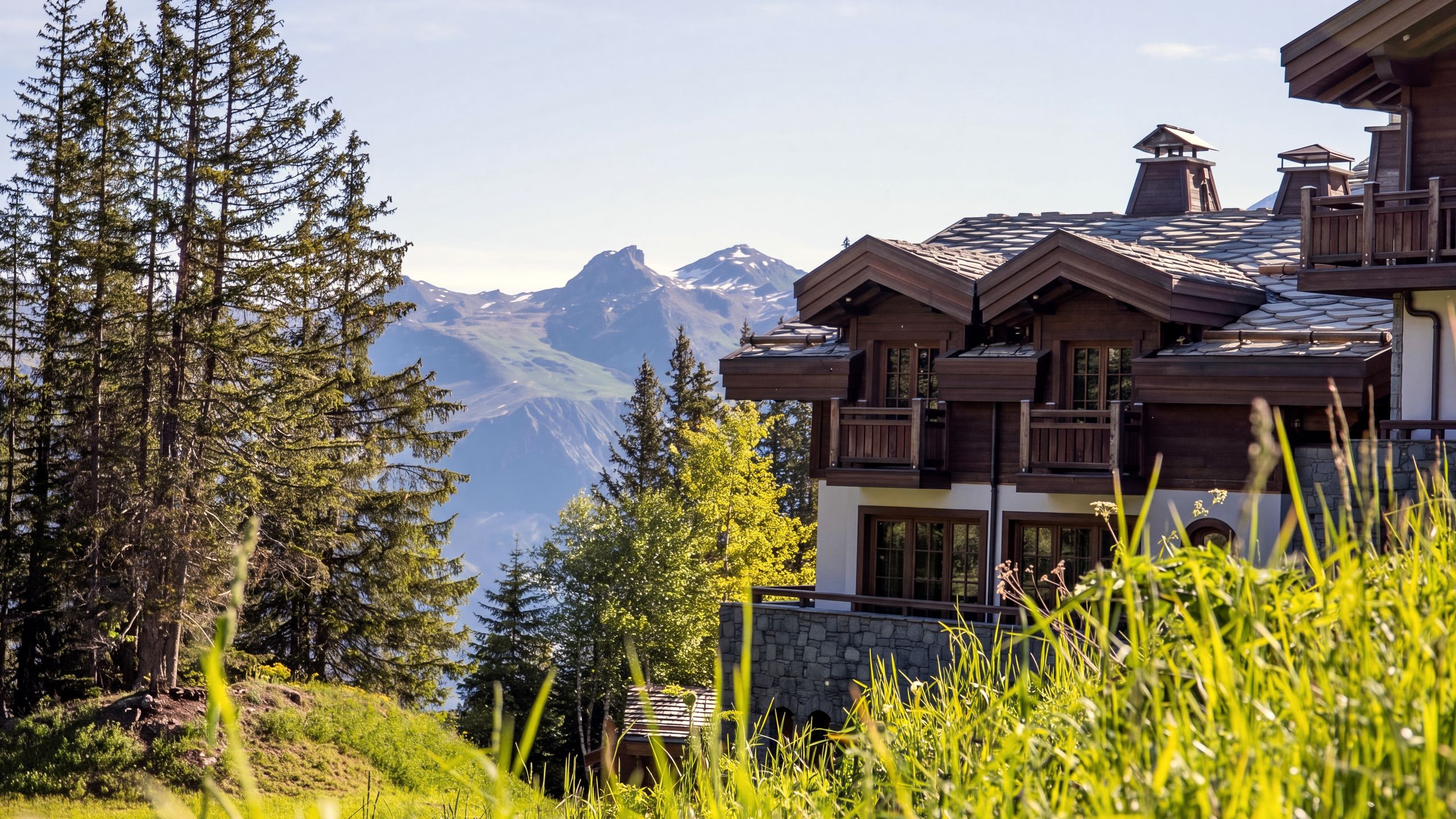 Un grand chalet de bois du Jardin Alpin, à Courchevel 1850, entre les sapins en été