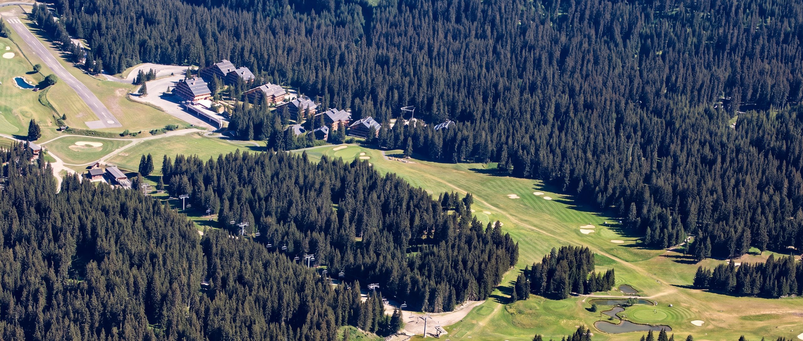 Vue aérienne de l'Altiport de Méribel en été : la piste d'aviation, les chalets et le golf dans la forêt