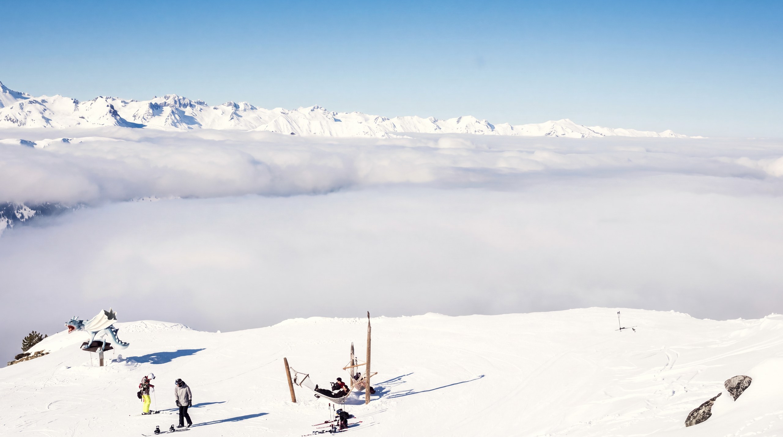 Des skieurs au sommet d'une piste, au-dessus d'une mer de nuages